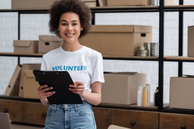 young african american volunteer with clipboard looking at camera in donation center