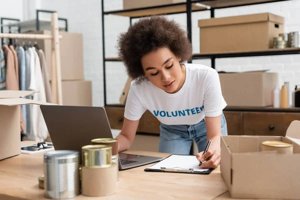 Joven Afroamericano Voluntario Escribir Portapapeles Cerca Computadora Portátil Centro Donación — Foto de Stock