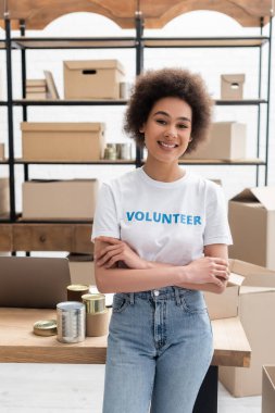 cheerful african american volunteer standing with crossed arms in charity warehouse