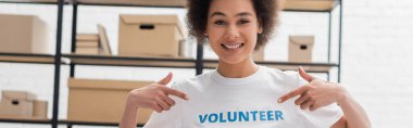 happy african american woman pointing at volunteer lettering on t-shirt, banner