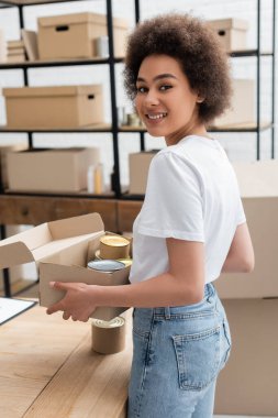 Afro-Amerikalı gönüllü, hayır kurumunda içinde konserve yiyecek olan bir kutu tutuyor.
