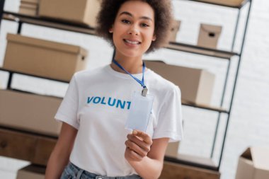 blurred african american volunteer showing empty id card in charity storehouse