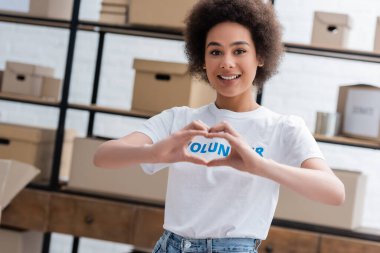 happy african american volunteer showing love sign at camera in charity center