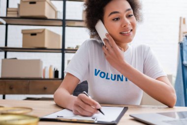 young african american woman talking on mobile phone near blurred clipboard in volunteer center