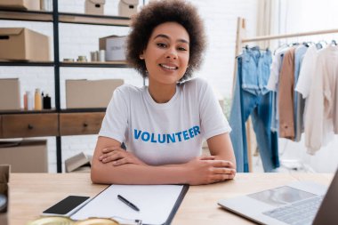 happy african american volunteer sitting at workplace in charity center