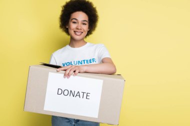 african american volunteer holding charity box with donate lettering isolated on yellow