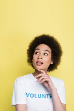 pensive african american volunteer touching chin and looking away isolated on yellow