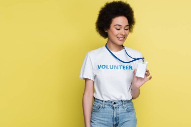 smiling african american volunteer showing blank name tag isolated on yellow