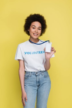 smiling african american volunteer showing empty name tag isolated on yellow
