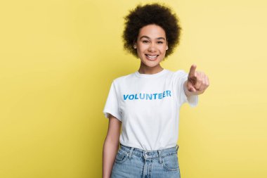 joyful african american volunteer pointing with finger at camera isolated on yellow