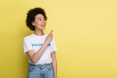 happy african american volunteer looking away and pointing with finger isolated on yellow