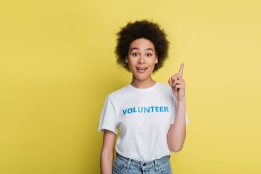 amazed and happy african american volunteer pointing up with finger isolated on yellow