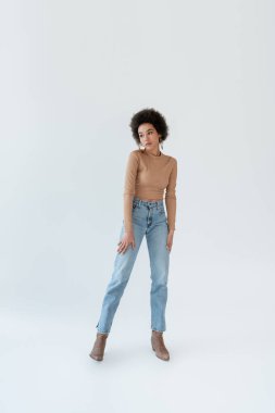 full length of african american woman in jeans and cowboy boots on grey background