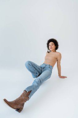 full length of african american woman in jeans and long sleeve shirt on grey background