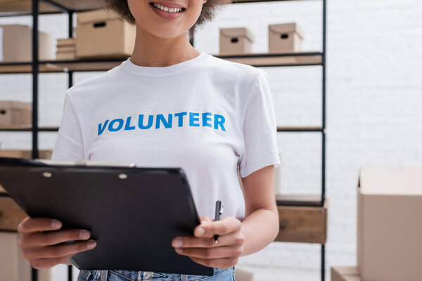 cropped view of african american volunteer holding clipboard in charity warehouse