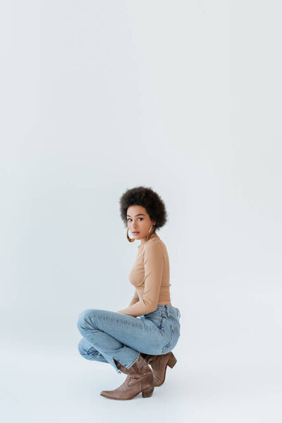 модная африканская американка в бежевой рубашке с длинным рукавом и джинсах позирует на сером фоне