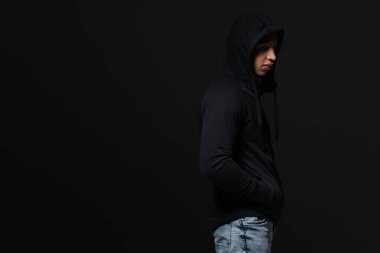 Side view of african american hooligan in hoodie standing isolated on black  clipart