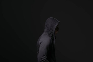 Side view of african american hooligan in hood standing isolated on black 