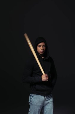 African american hooligan holding baseball bat and looking at camera isolated on black  clipart