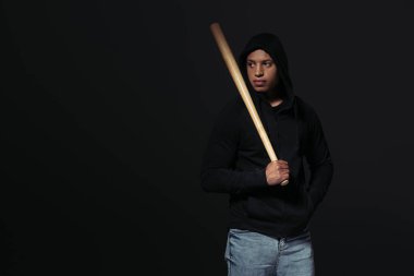 African american hooligan with baseball bat looking away isolated on black  clipart