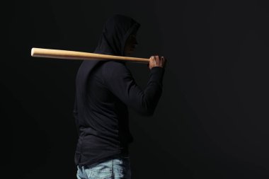 Side view of african american hooligan holding baseball bat isolated on black  clipart