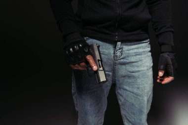 Cropped view of african american hooligan holding gun on black background 