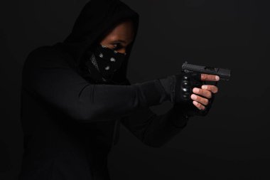 African american bandit in mask holding handgun isolated on black  clipart