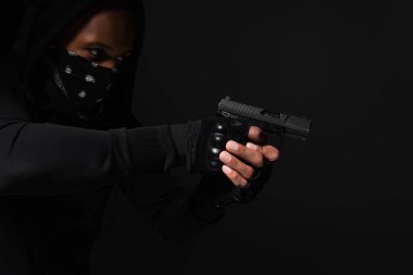 African american bandit with obscure face holding handgun isolated on black  clipart