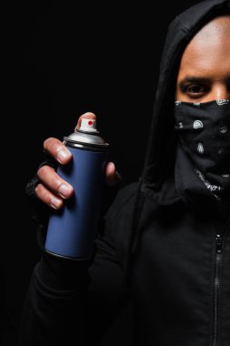 Cropped view of african american bandit with mask on face holding spray paint isolated on black  clipart