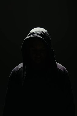Silhouette of hooligan in hood standing in lighting isolated on black  clipart