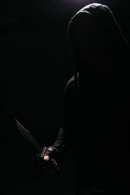 Kapüşonlu haydutların silueti siyah ışıkta izole edilmiş bir bıçak tutuyor. 