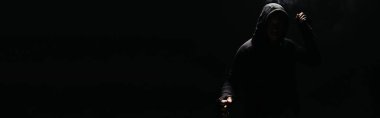 Silhouette of african american bandit in hoodie and gloves holding knife isolated on black, banner 