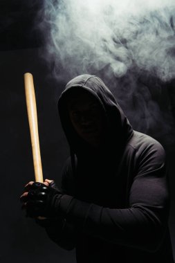 Silhouette of african american bandit in hood holding baseball bat on black background with smoke  clipart