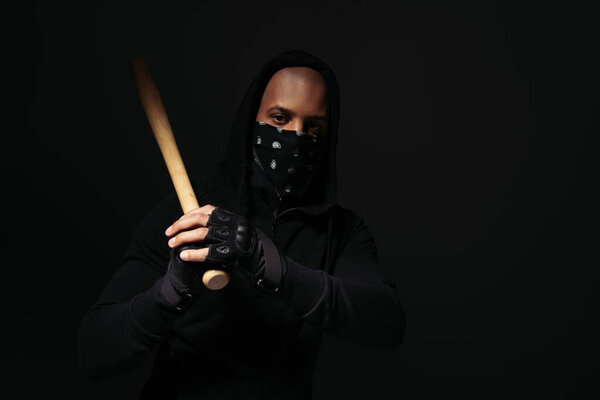 African american hooligan in mask on face and glove holding baseball bat isolated on black 