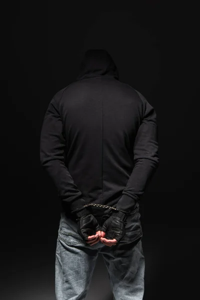 Back view of african american bandit in hoodie and handcuffs standing isolated on black