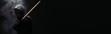 Side view of silhouette of african american hooligan with baseball bat on black background with smoke, banner  