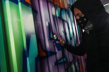 Yüzünde maske olan, duvara grafiti çizen Afro-Amerikan vandalının yan görüntüsü 