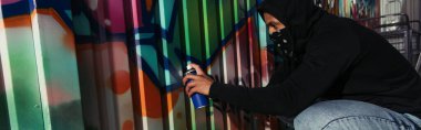 Side view of african american vandal with obscured face drawing graffiti on wall, banner 