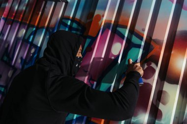 Side view of african american vandal drawing graffiti on wall outdoors at night 
