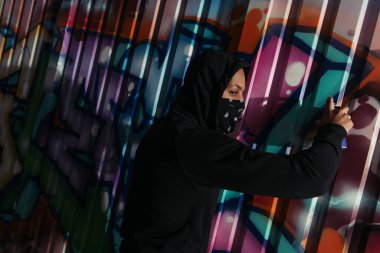 Side view of african american vandal looking away while drawing graffiti on wall outdoors at night 