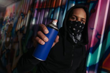 Blurred african american vandal holding spray paint near graffiti on wall 