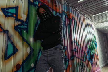 Maskeli ve kapüşonlu Afro-Amerikan vandalları duvardaki duvar yazısının yanında kollarını kavuşturuyorlar. 