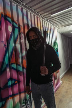 African american vandal holding baseball bat near graffiti on wall 