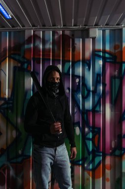 Maskeli Afrikalı Amerikalı holigan duvarda duvar yazısı olan beyzbol sopası tutuyor. 
