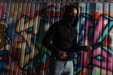 Kapüşonlu Afrikalı Amerikalı holigan elinde beyzbol sopasıyla duvarda grafiti yapıyor. 