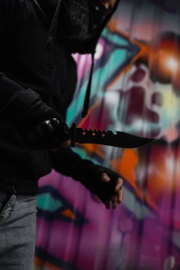 Afro-Amerikalı soyguncunun açık havada duvardaki bulanık duvar yazısının yanında bıçak tutarken çekilmiş görüntüsü. 