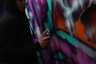 Cropped view of african american vandal painting graffiti on wall on urban street 