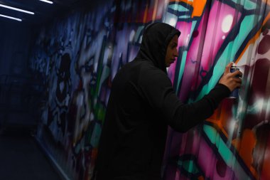 Side view of african american vandal painting graffiti on wall 