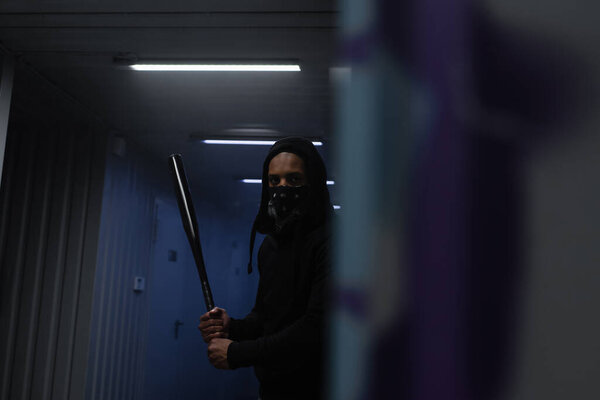 Африканский американский вандал держит бейсбольную биту у стены гаража