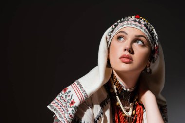 portrait of young ukrainian woman in traditional clothing with ornament and red beads looking up on black 